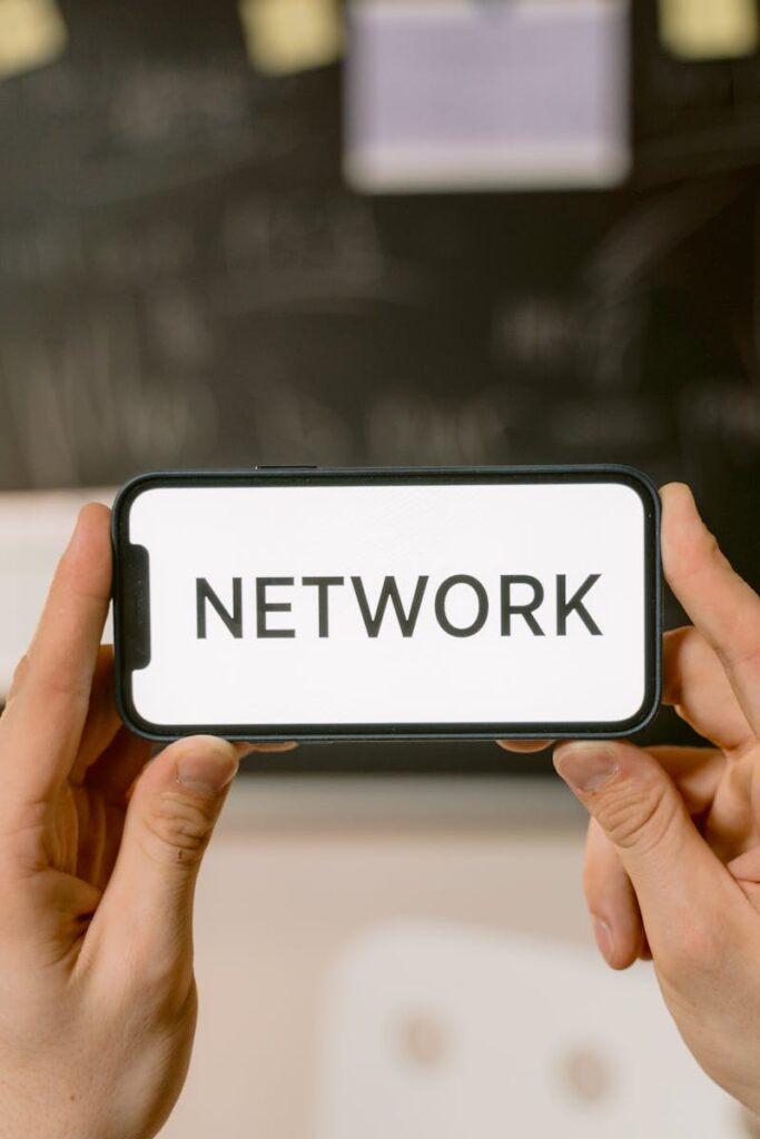 pexels-photo-6914350-6914350-1 Close-up of hands holding a smartphone showing the word 'Network' on screen.